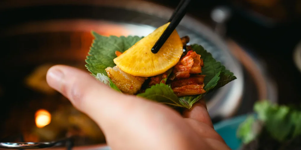 Close-up of a hand holding a small leaf-wrapped snack topped with a slice of banana