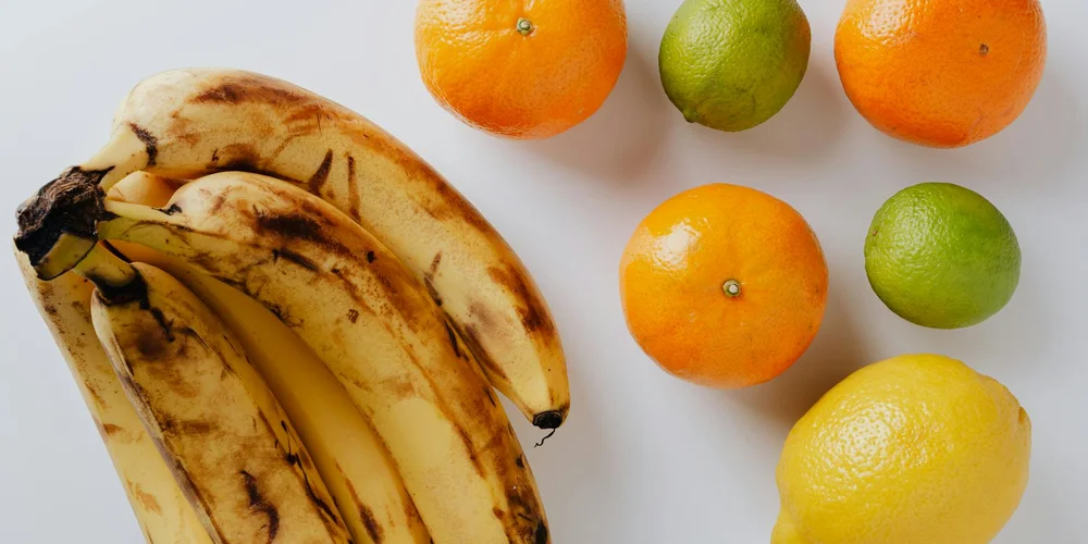 Bananas on the left with oranges, limes, and a lemon on a white surface