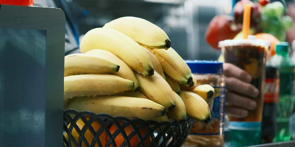 A basket of bananas on a table with colorful beverages blurred in the background, suggesting tempting snacks and cravings.