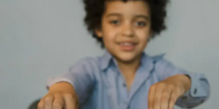 Smiling child extending hands toward the camera in a light blue shirt, against a neutral background.
