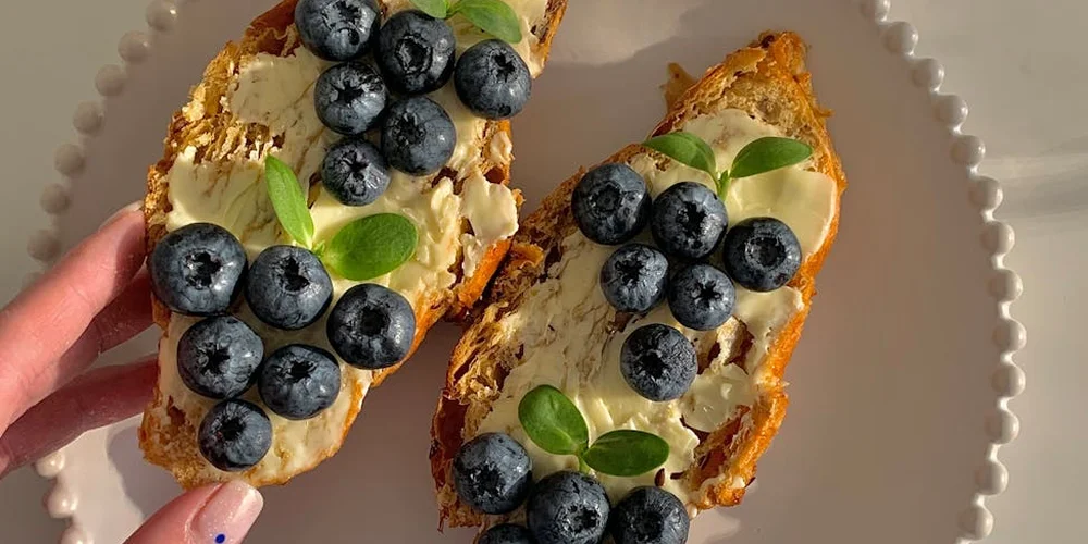 Two slices of toasted bread topped with cream cheese, blueberries, and fresh basil on a plate.