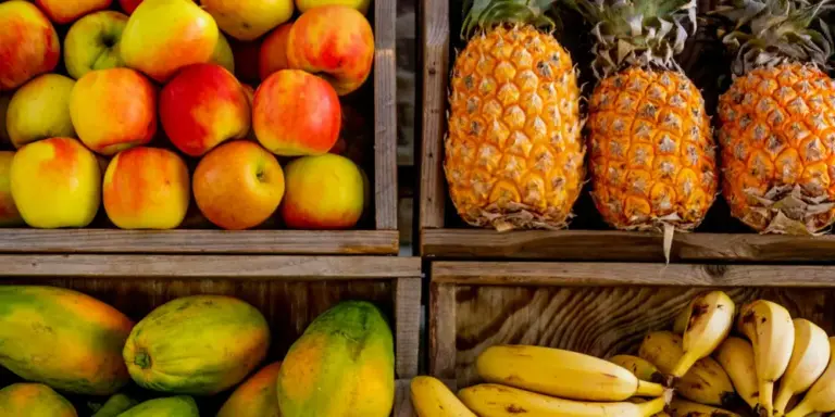 Assorted fruits in wooden crates: apples, pineapples, mangoes, and bananas