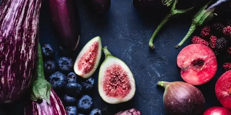 A selection of fruits and vegetables on a dark surface, including figs, blueberries, an eggplant, and apples, prepared as foods for terrestrial turtles.