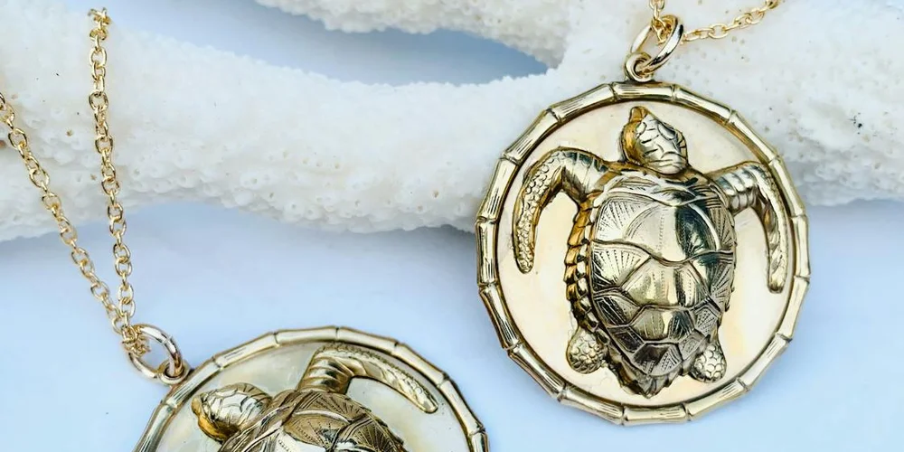 Gold and silver turtle pendant necklaces resting on a light blue surface.