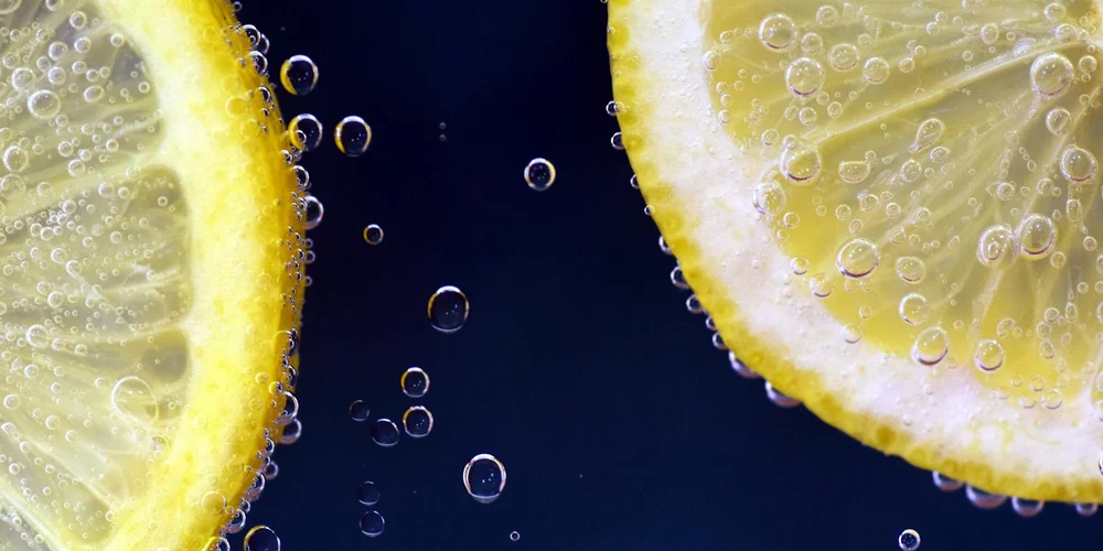 Two lemon halves with bubbles in water against a dark blue background.
