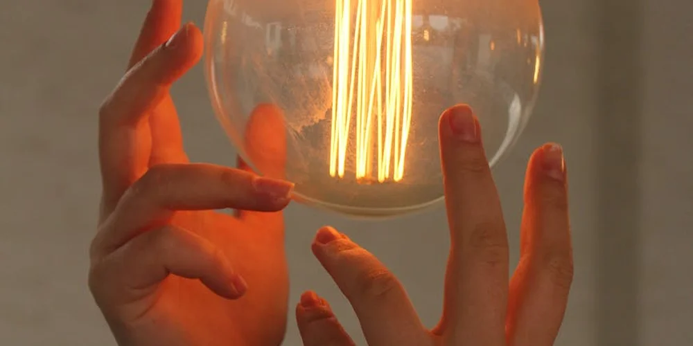 Close-up of a glowing filament light bulb held by hands, illustrating monitoring and fine-tuning of a tortoise habitat's lighting.