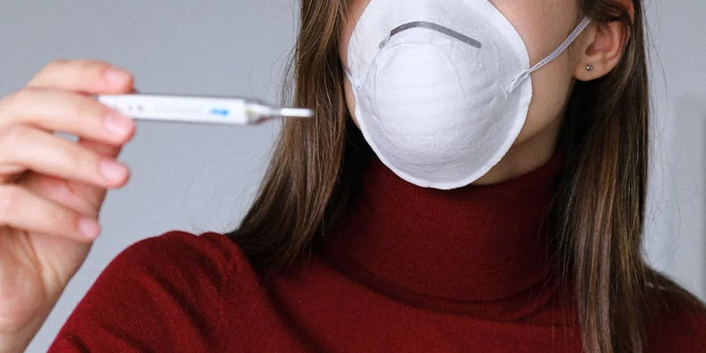 Person wearing a face mask holds a thermometer to measure the temperature in a turtle's habitat.