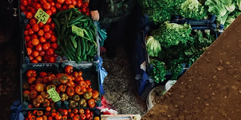 Fresh market produce including red tomatoes, green beans, leafy greens, and peppers displayed in crates.