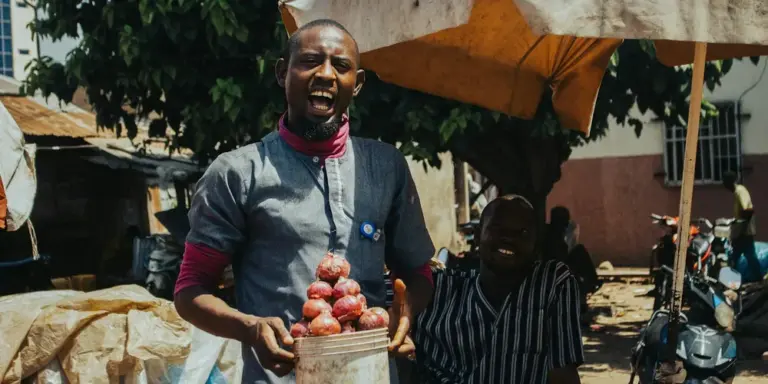 Market vendor holding a basket of red onions in a busy outdoor market