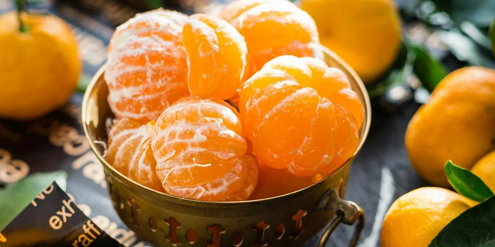 A bowl of peeled mandarin oranges surrounded by whole oranges.