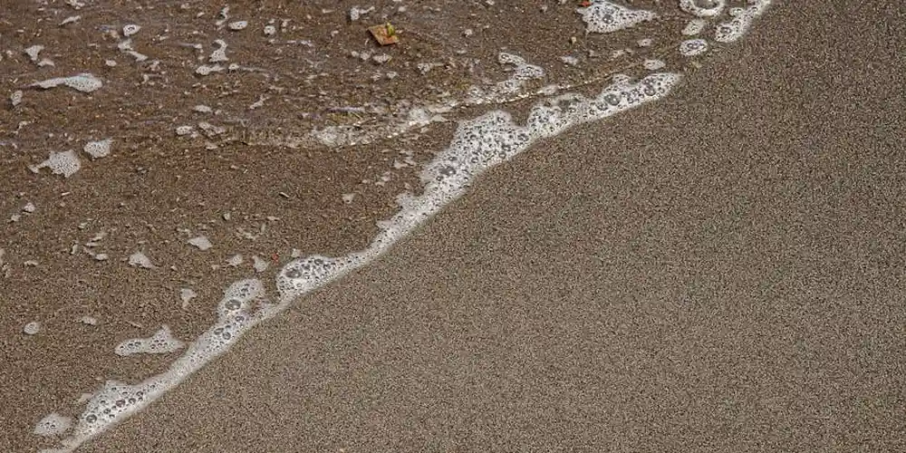 Close-up view of waves washing onto a sandy beach with foamy white surf