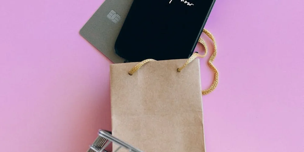 Brown paper shopping bag on a pink background with a smartphone resting on top