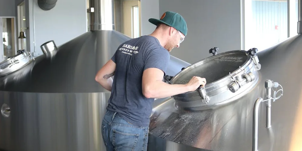 Person wearing a cap inspecting a large stainless steel stock tank in a workshop.