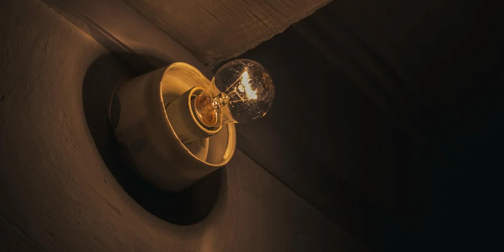A single incandescent bulb mounted in a ceramic fixture on a dark wall, illustrating a simple heating/light setup.