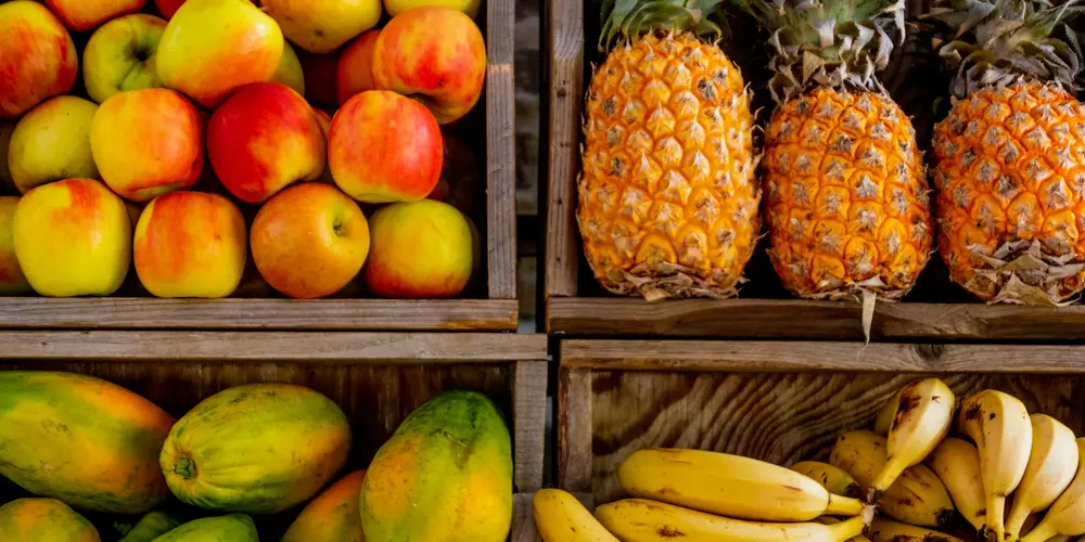 Assorted fresh fruits including apples, pineapples, and bananas arranged in wooden crates, showing different portion options for turtle meals.