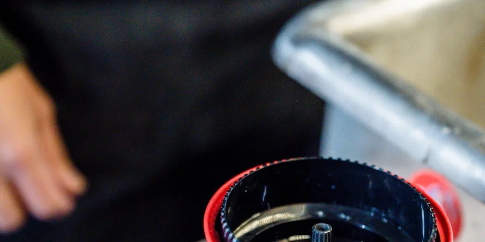 Close-up of a black canister-style filtration component with a red end cap on a work surface; a person's hand is visible in the background, illustrating hands-on sump upgrades for a turtle tank.