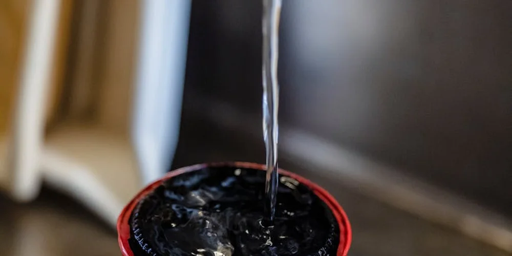 Close-up of a water stream pouring into a dark turtle tank or basin with a red rim, illustrating the cleaning process.