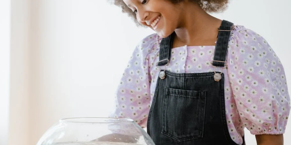 Person smiling and looking down, wearing a purple polka-dotted blouse and black overalls