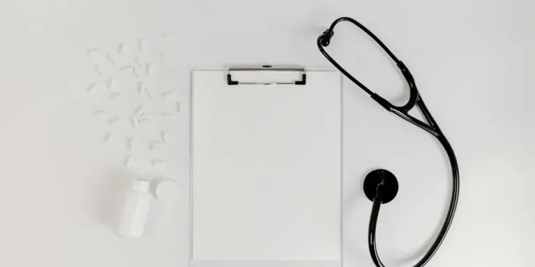 Stethoscope resting on a white clipboard with a small medicine bottle nearby on a clean clinical examination table.