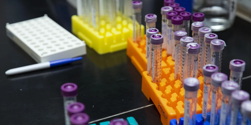 Lab scene with multiple test tubes in orange racks, a yellow rack in the background, a white pen, and a white tube rack on a black lab bench, illustrating water-quality testing for a turtle tank.