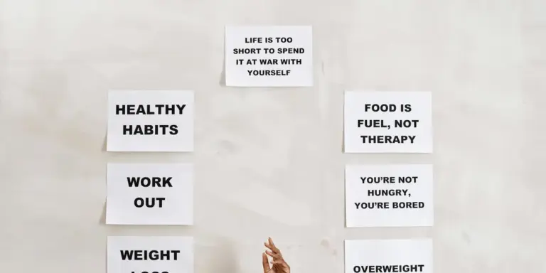 Light-colored wall with several sticky notes arranged in two columns, showing phrases such as HEALTHY HABITS, WORK OUT, WEIGHT, FOOD IS FUEL, NOT THERAPY, and YOU'RE NOT HUNGRY, YOU'RE BORED, plus a top note reading LIFE IS TOO SHORT TO SPEND IT AT WAR WITH YOURSELF.