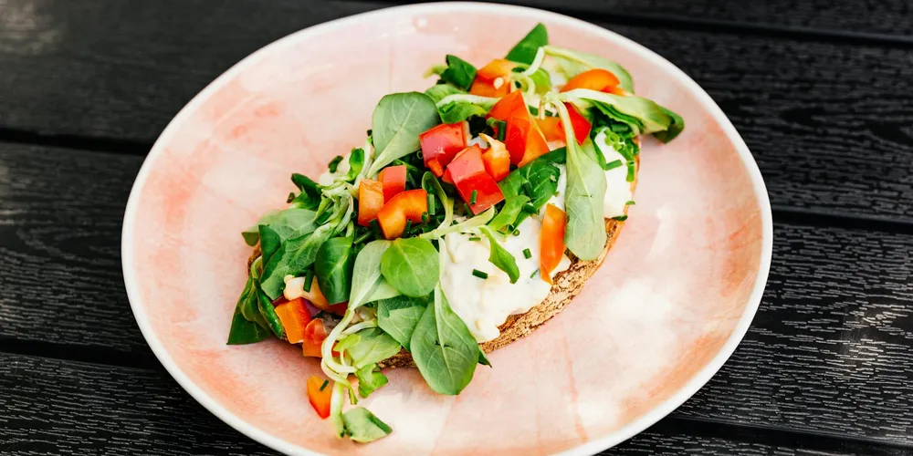 Open-faced toast topped with leafy greens and diced red and orange peppers on a pink plate