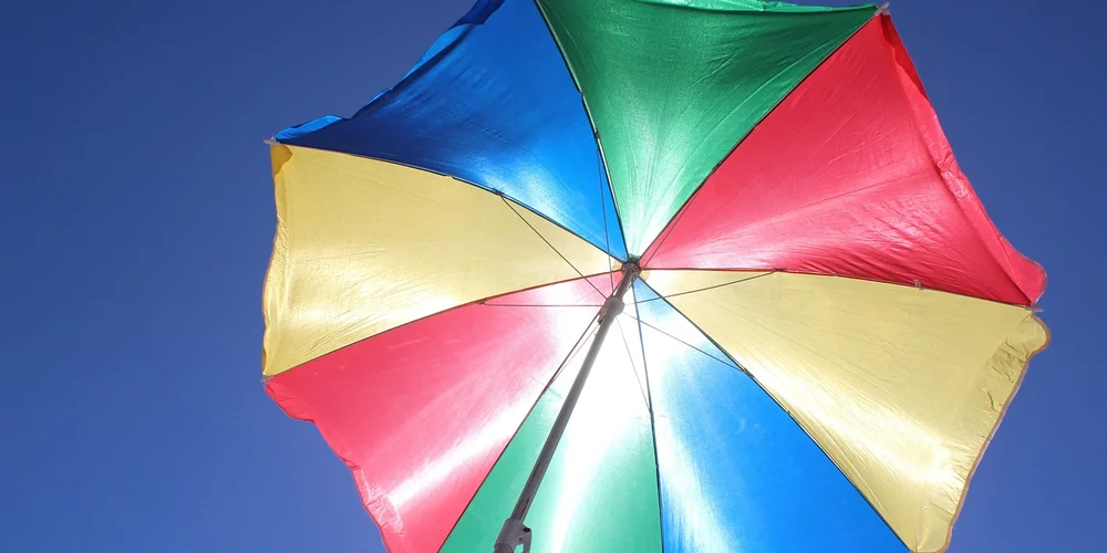 A colorful, multi-panel umbrella opened outdoors against a clear blue sky.