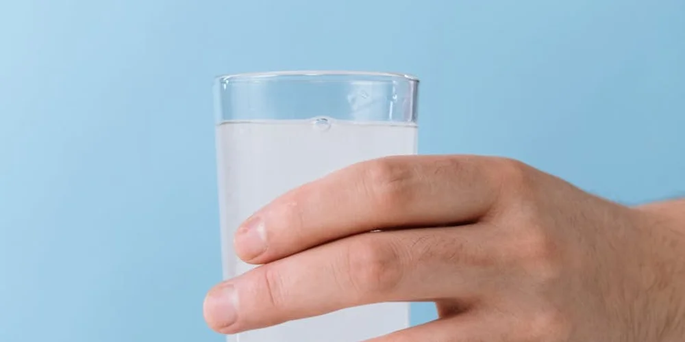 Close-up of a hand holding a glass of water against a blue background