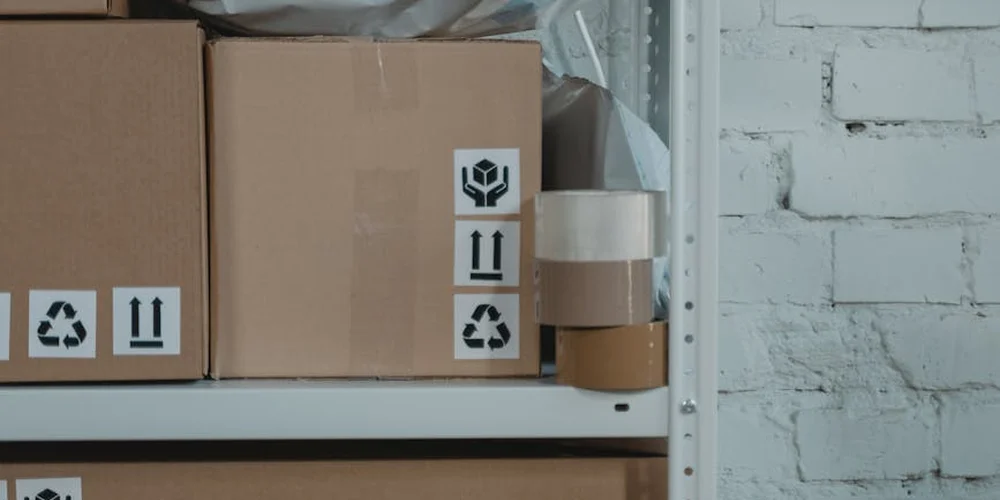 Cardboard boxes on metal shelving in a storage area, with packing tape and labels visible.