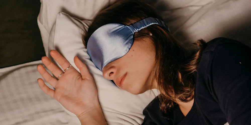 Person sleeping in bed with a blue sleep mask